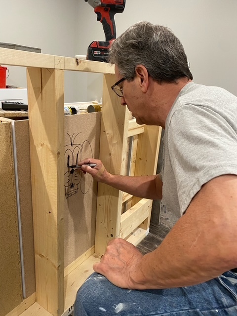 Bill drawing his trademark dog on a wooden frame.